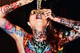 A tattooed woman swallows two swords with golden hilts.