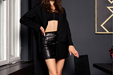 A young woman wears a black leather mini skirt and a half shirt that reveals a flat torso.