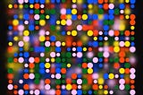 Random pink, blue, red, green, and yellow dots, of varying sizes and resolution on a black background.