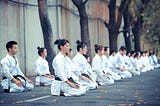 A row of people in karate uniforms sitting in meditation position