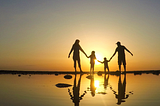 Family of 4 walking in the sea and sun set