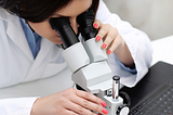 A photo of a woman looking through a microscope.