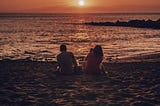 silhouette of a sitting couple looking out into the sunsetting over the calm ocean