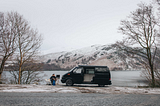 Micro camper by lake with man sat outside in snow