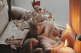 Cozy scenery of candles, a sweater, a book, and fall plants.