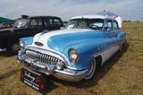 A 1953 Buick Sedan which was famous for having a V8 engine parked in a field at a car show. It is very similar to the Buick my brother and I used to work on together.