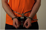 A man handcuffed man in an orange shirt and black bottoms