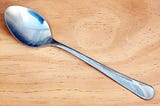 A dessert spoon with a shiny patina against a wooden background