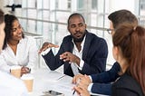 Millennial employees gathered in boardroom for training, black man speaking to Black and white co-workers and corporate team.