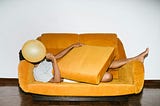 A woman lying on a sofa, trying to hide behind sofa cushions and a ballon