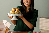 smiling woman holding a cake plate piled with scones