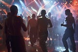 a dimly-lit dance floor with shirtless guys dancing under strobe lights