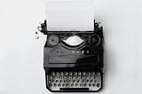 Photo by Florian Klauer on Unsplash. The image is a black old manual typewriter with a piece of paper in it.