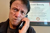 Photo of author on a cordless phone in front of his Cornell MBA diploma