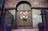 A large wooden door inside a gated building with a ‘no turtles allowed’ sign on top of it