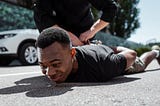 selective focus of detained Black man lying on street near policeman, racism concept