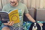 Ash holding his book Unforgettable Encounters, seated next to a dog looking a the camera