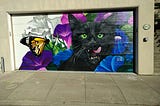 A mural on a garage of a black cat licking its lips as a monarch butterfly floats by.