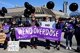 Members of the Tri-Cities Community Action Team are holding black balloons and a big purple sign with the words #End Overdose.