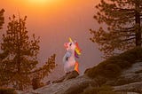 A person in a unicorn costume stands on top of some boulders overlooking a wooded valley during sunset.
