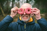 A happy middle-aged man holding donuts up to his eyes like they are eyeglasses.