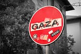 A red stop sign with the word Gaza across the white bar in middle against a black and white background of houses and trees