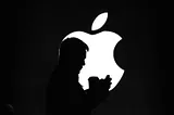 Silhouette of man using phone before a glowing Apple logo