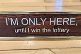 Desk placard reading “I’M ONLY HERE, until I win the lottery”. That’s one strategy, sure