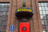 brick building with windows, a red door, and a neon sign that says, “El Gaucho”