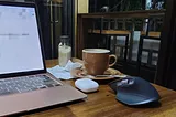 Macbook Air, a cup of coffee and a mouse on a wooden table.