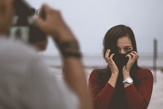 woman hiding her face while a person takes a photograph of her
