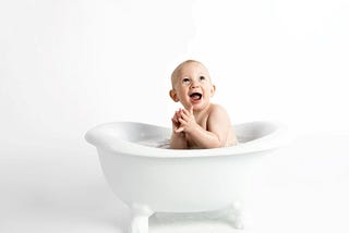A baby boy sitting in a white clawfoot tub.