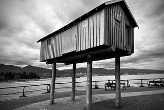 House on stilts against mountain and ocean backdrop. Black and white photograph.
