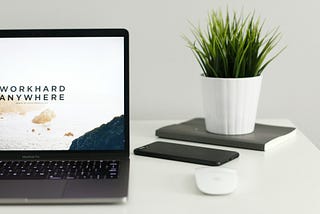 IMAGE: An open laptop with the words “Work hard anywhere” on the screen, and a potted plant on the side