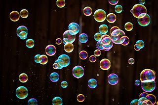 Many iridescent soap bubbles glimmering in darkness.