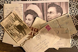Closeup of a few old faded photos of a happy young couple and scattered envelopes and letters on a white doily on an old wood table.