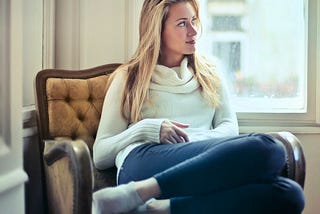 A woman with long blonde hair wearing a white sweater, with an amused look on her face.