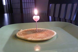A lit “happy birthday” candle in a pancake.