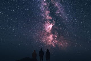 A starry night sky with a silhouette of 3 people stargazing