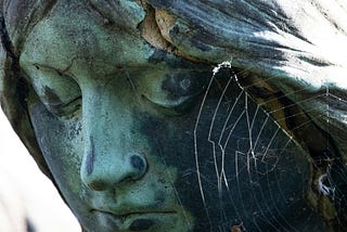 Close up of a statue of a woman with a spider web on her face