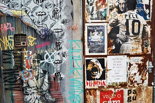 Photo of a wall outside that is covered with stickers and political posters with punk themes by Mínimo on Unsplash