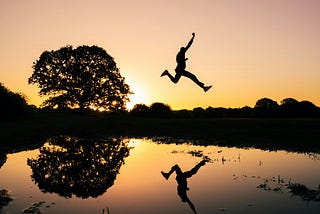 A man jumps for joy, silhouetted against the morning sun