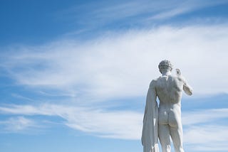 statue of naked man holding clothing from behind, blue sky