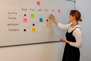A woman plans her weekly workflow on a whiteboard