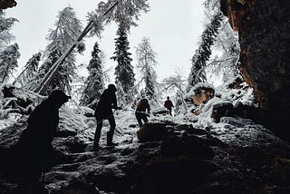4 people in line holding rope climbing out of a cave.