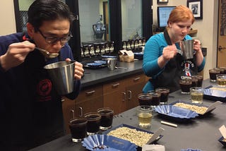 Two people tasting coffee with samples of green beans on the table