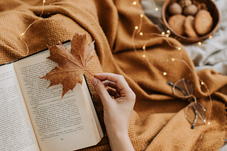 Book, lights, and glasses on a blanket. Hand hold a leaf.