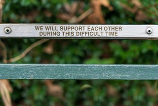 metal bar stating “we will support each other during this difficult time” Photo by <a href=”https://unsplash.com/@jannerboy62?utm_content=creditCopyText&utm_medium=referral&utm_source=unsplash">Nick Fewings</a> on <a href=”https://unsplash.com/photos/brown-wooden-bench-with-quote-KUCyZtjKqwA?utm_content=creditCopyText&utm_medium=referral&utm_source=unsplash">Unsplash</a>