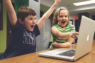 A photo of two happy, excited children pointing to a computer display.