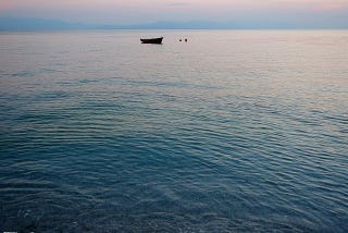 Photo of the sea at the end of the day with a small boat in the distance.